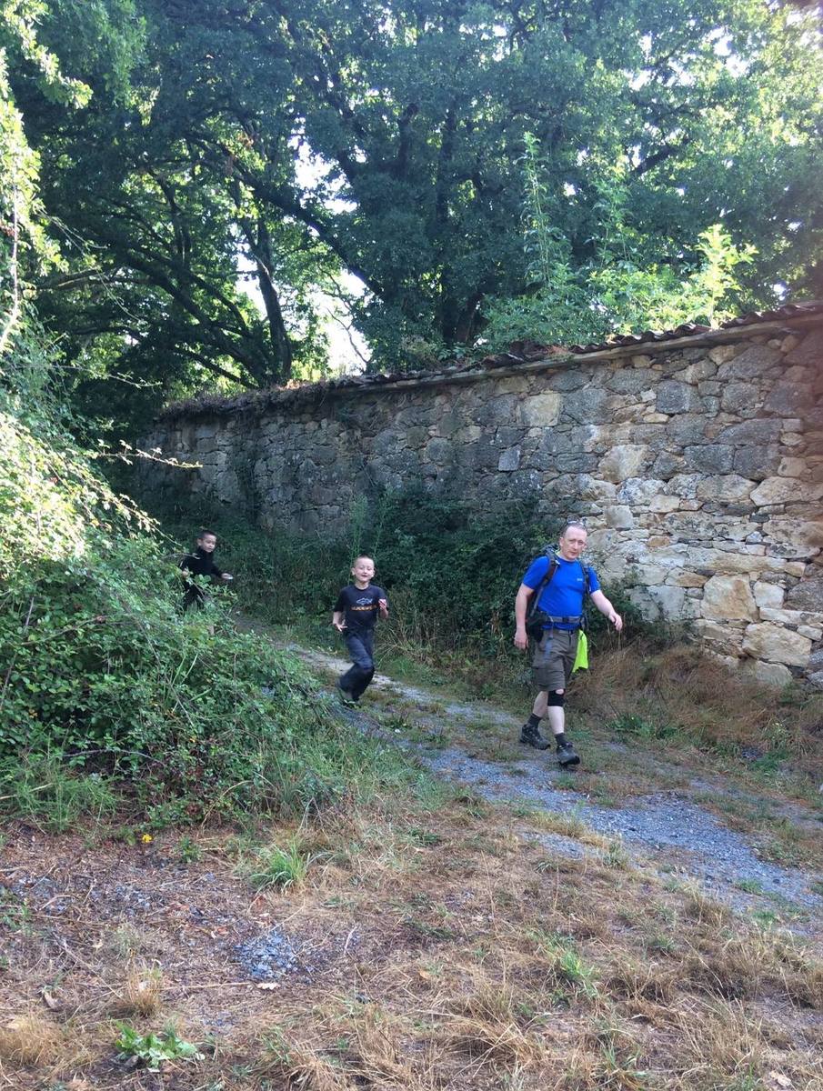 Peter walking a gravel lane beside a long stone wall, with two young boys running along behind him.