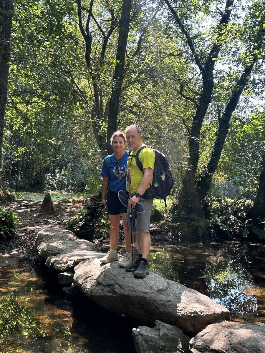 Peter and a fellow walker standing on large flat stones that cross a shaded stream.