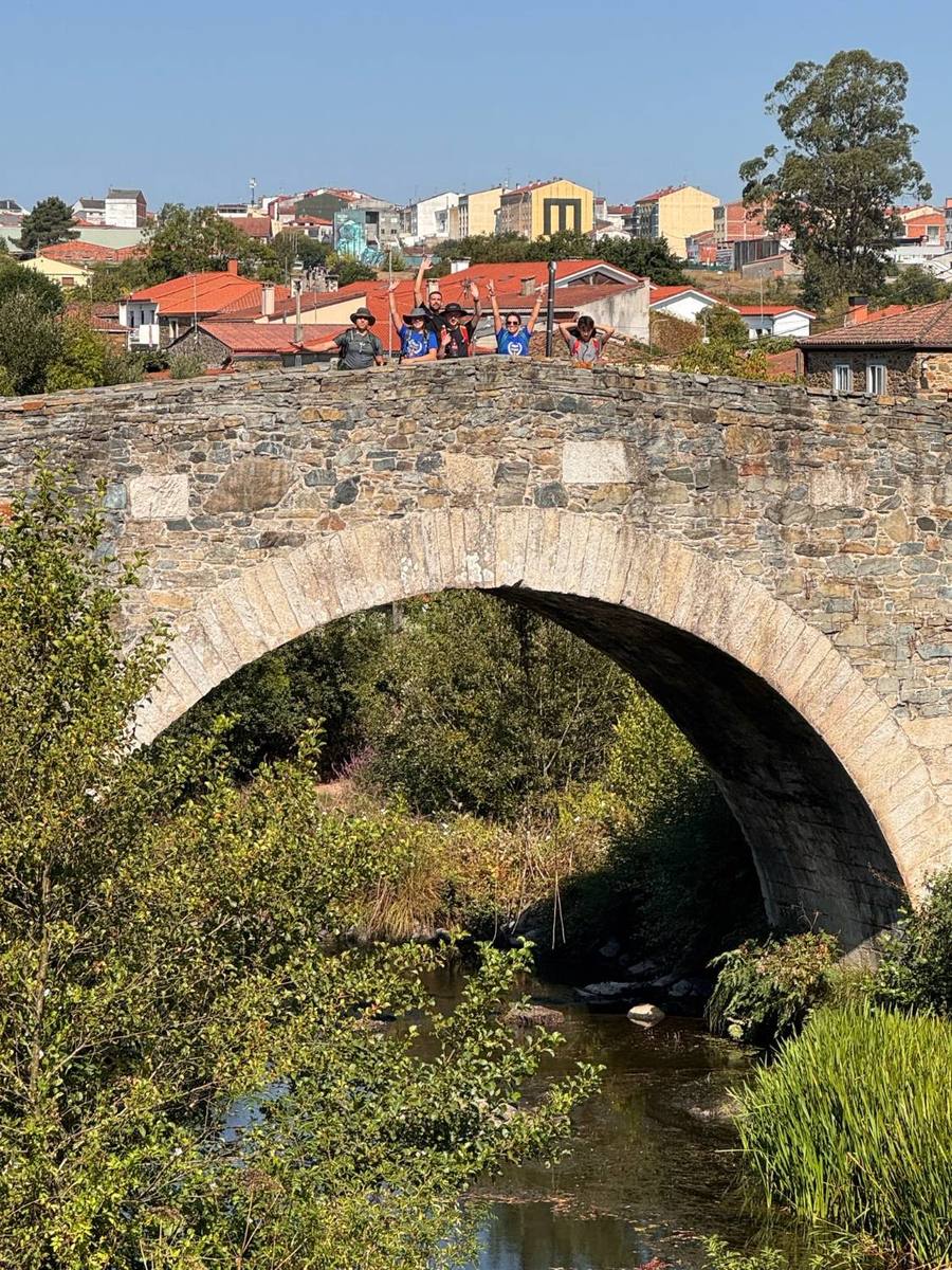 The group waving with arms raised from the top of an old arched stone bridge.