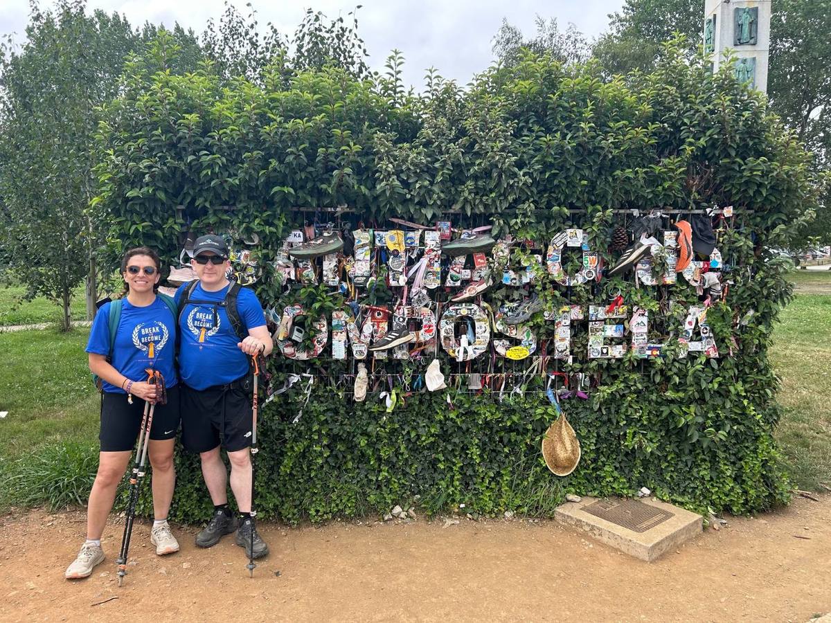 Peter and a fellow walker beside the Santiago de Compostela sign, covered in stickers and shoes left by pilgrims.